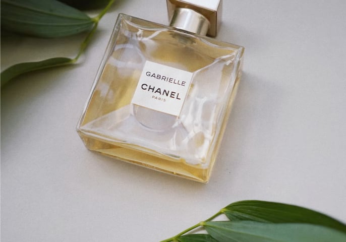 Gabrielle Essence perfume bottle laying flat on a table with leaves around it